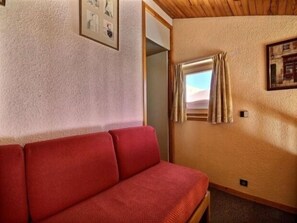 Ein Zimmer mit einem roten Sofa, einem gerahmten Bild an der Wand und einem Fenster mit Vorhängen.