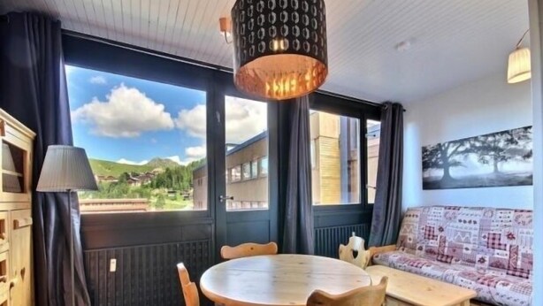 Een gezellige kamer met een houten eettafel en stoelen, een bank, en een groot raam met uitzicht op een berglandschap.