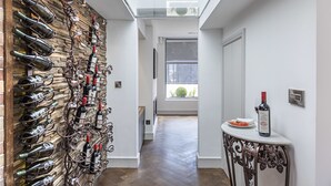 Un pasillo con una alacena para vinos a la izquierda, una mesa con una botella a la derecha y vistas al exterior a través de una ventana.
