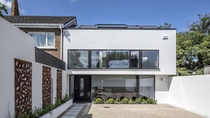 Una casa moderna de dos pisos con un amplio frente de vidrio y un dormitorio visible en el nivel superior.
