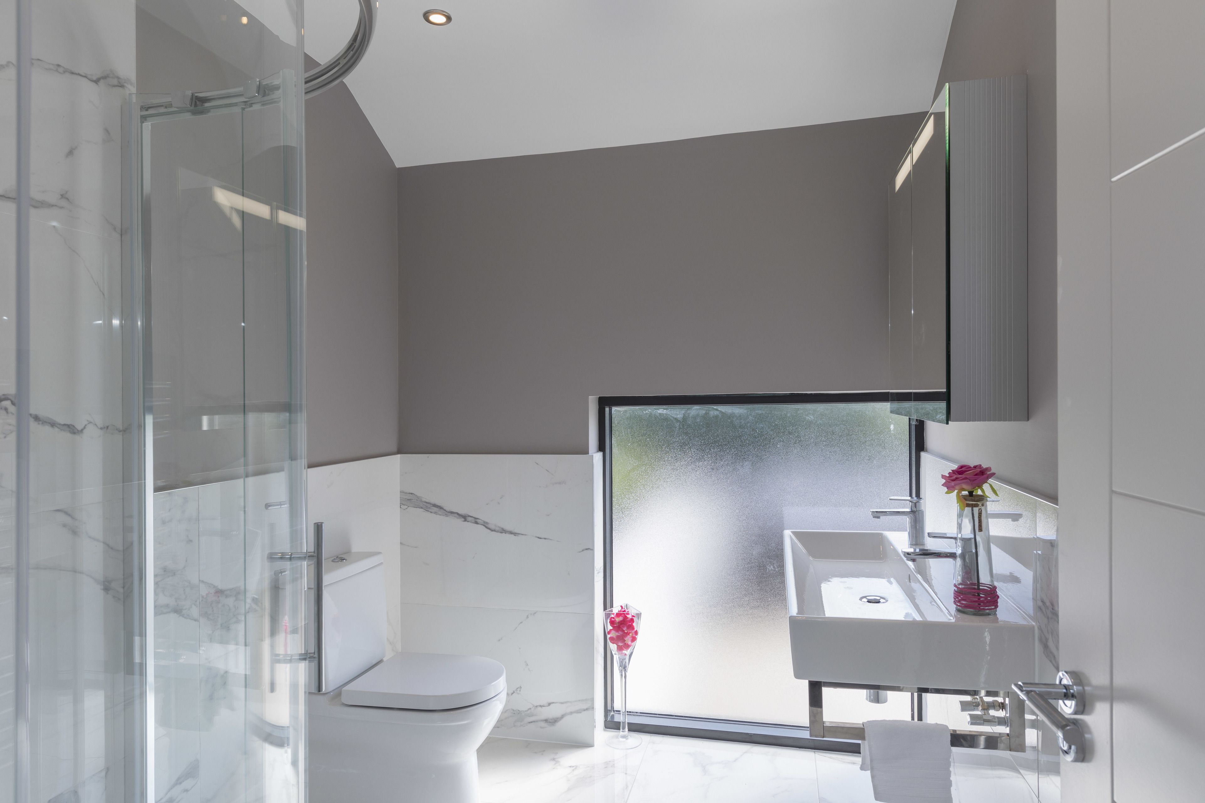 Een moderne badkamer met een glazen douchecabine, toilet en een wastafel met spiegel erboven.