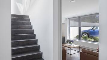 Een modern interieur met een trap naar een leefruimte, een groot raam met uitzicht op een auto en een kleine tafel met een bloevas.