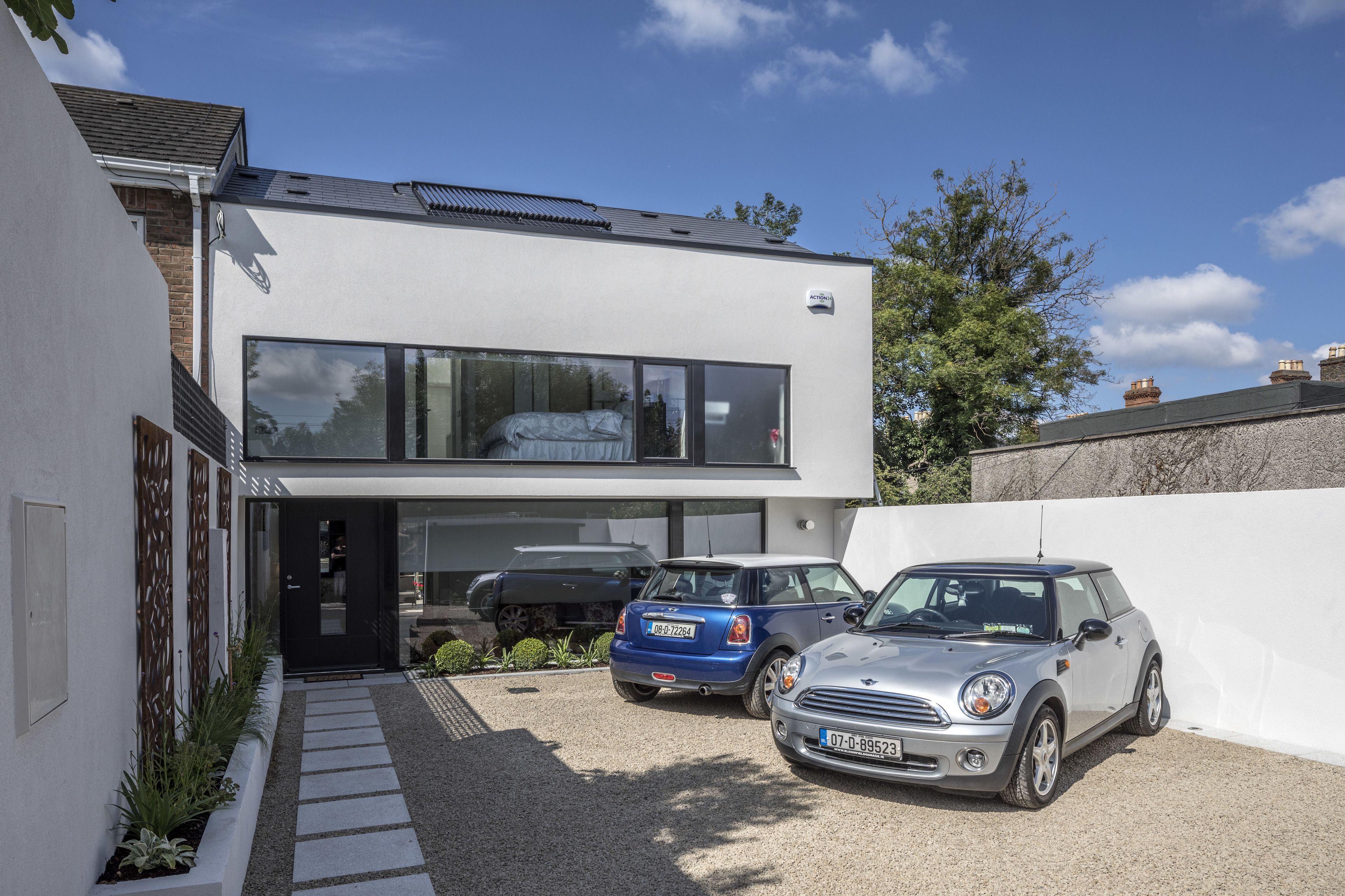 A modern two-story house with a garage, two cars parked in the driveway, and a clear blue sky.