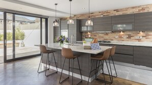 Una cocina moderna con una isla grande, taburetes de bar, iluminación colgante y vistas al exterior.