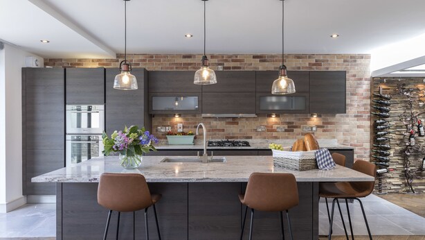 Una cocina moderna con una isla grande, muebles oscuros y lámparas colgantes.
