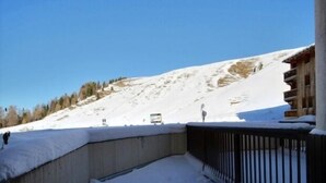 En snötäckt sluttning med en träbyggnad och ett fordon i bakgrunden.