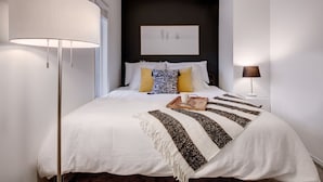 A neatly arranged bedroom with a large bed, a bedside lamp, and a framed picture on the wall.