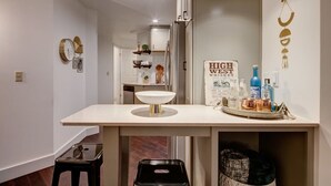 A modern kitchen with a white countertop, a sink, and a tray of whiskey bottles.