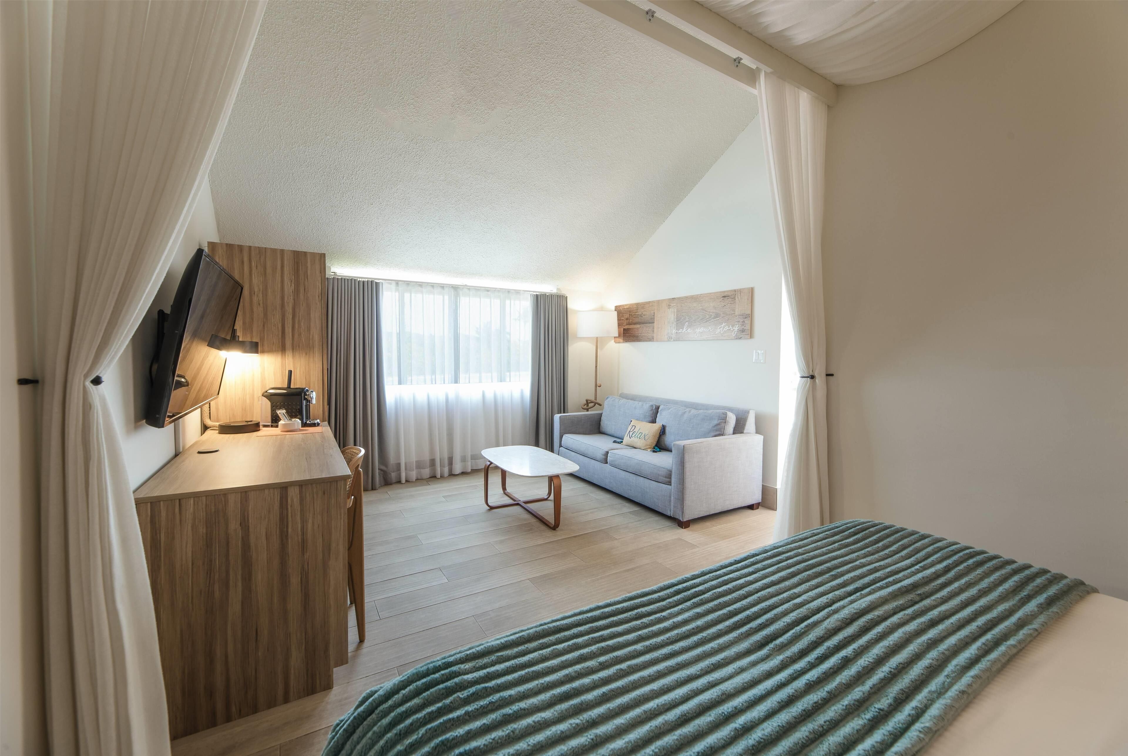 Una habitación de hotel moderna con un escritorio de madera, un sofá, una cama con manta a rayas y un televisor de pantalla plana.