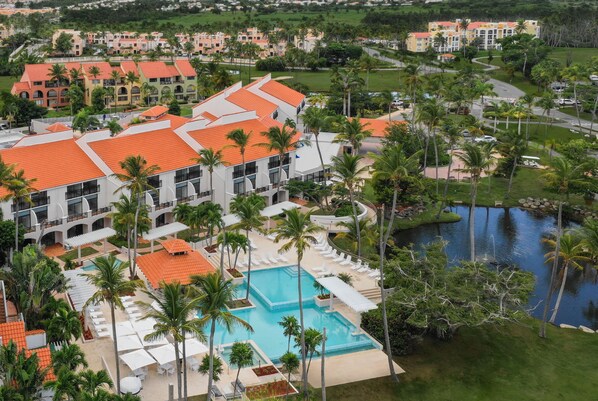 A resort with a swimming pool, palm trees, and a large building with a red roof. - Wyndham Palmas Beach and Golf Boutique Resort (Humacao)