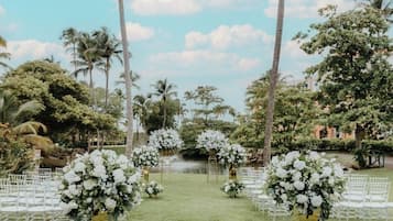 An outdoor wedding venue with white floral arrangements, palm trees, and a clear sky.
