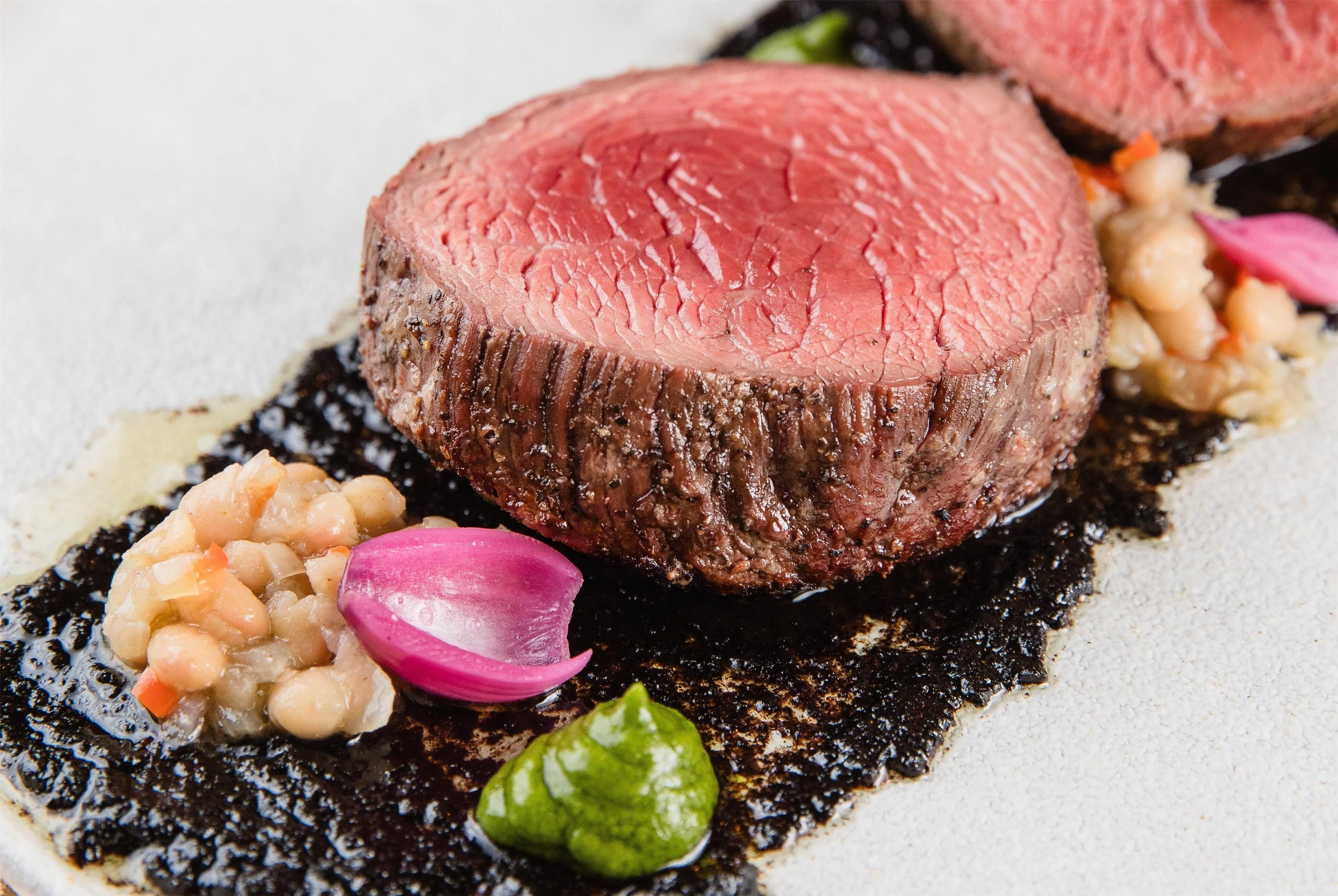 Un filete con salsa oscura, adornado con vegetales encurtidos y salsa verde.