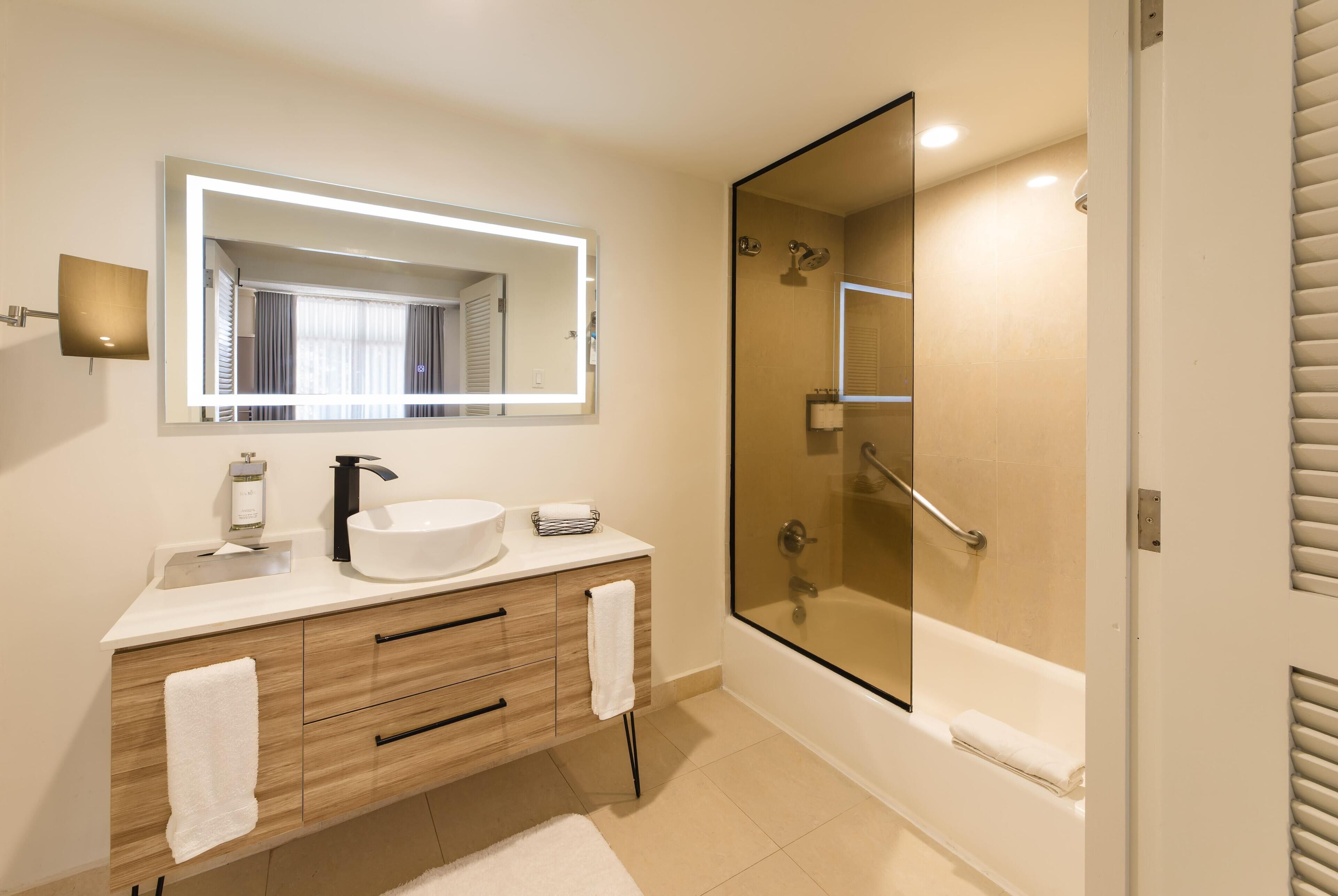Een moderne badkamer met een grote spiegel, een wastafel, een badkamerkast met lades, een douche met glazen wanden en een bad.