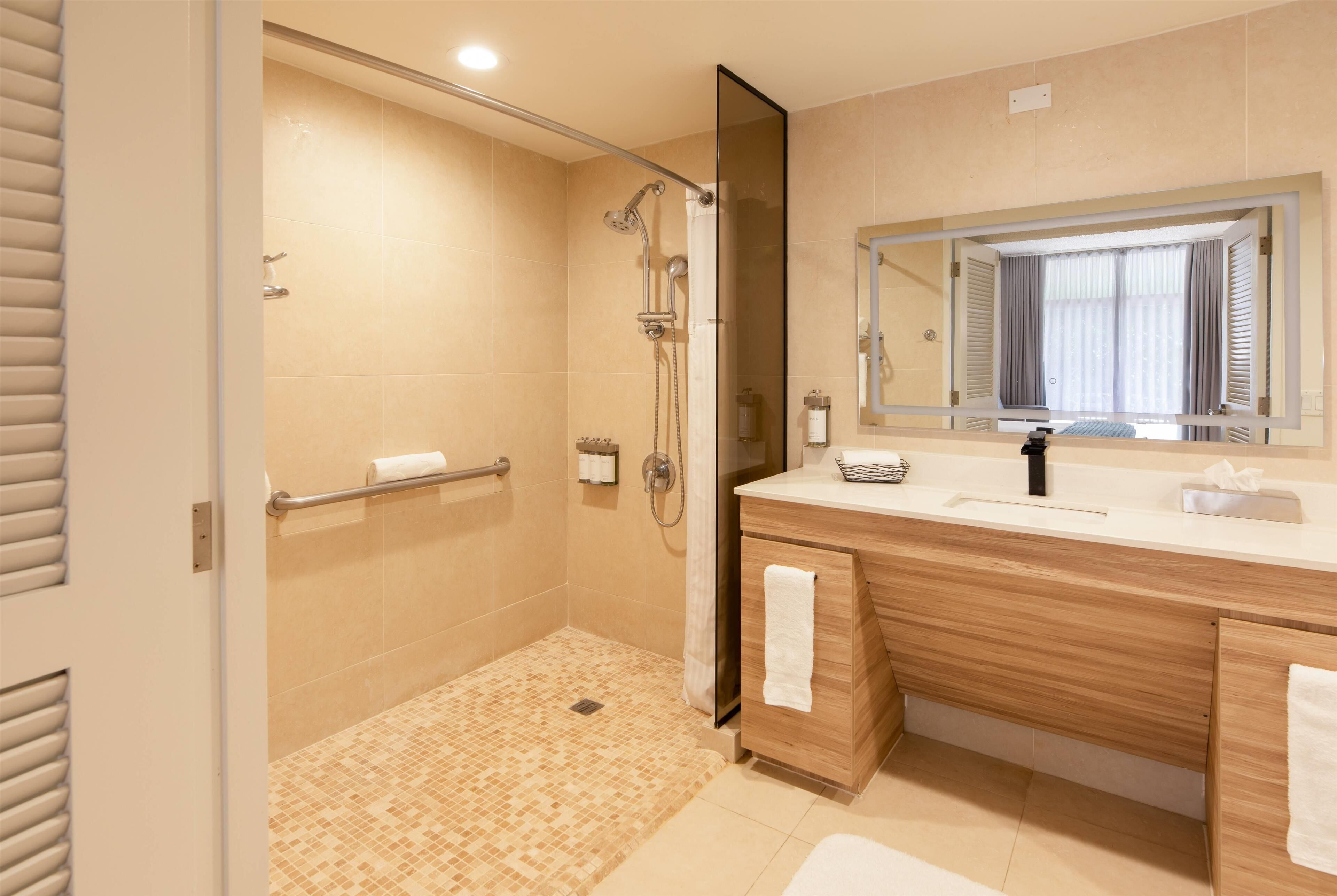 Ein modernes Badezimmer mit bodengleicher Dusche, Holzwaschtisch, großem Spiegel und Handtuchhalter.