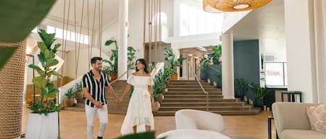 A spacious lobby with a staircase, potted plants, and modern furniture.
