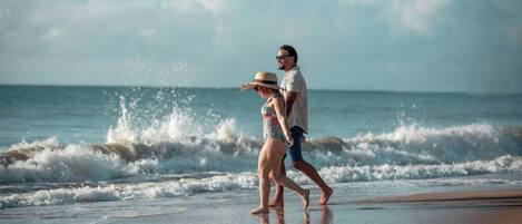 Ein Paar spaziert am Strand, im Hintergrund brechen Wellen.