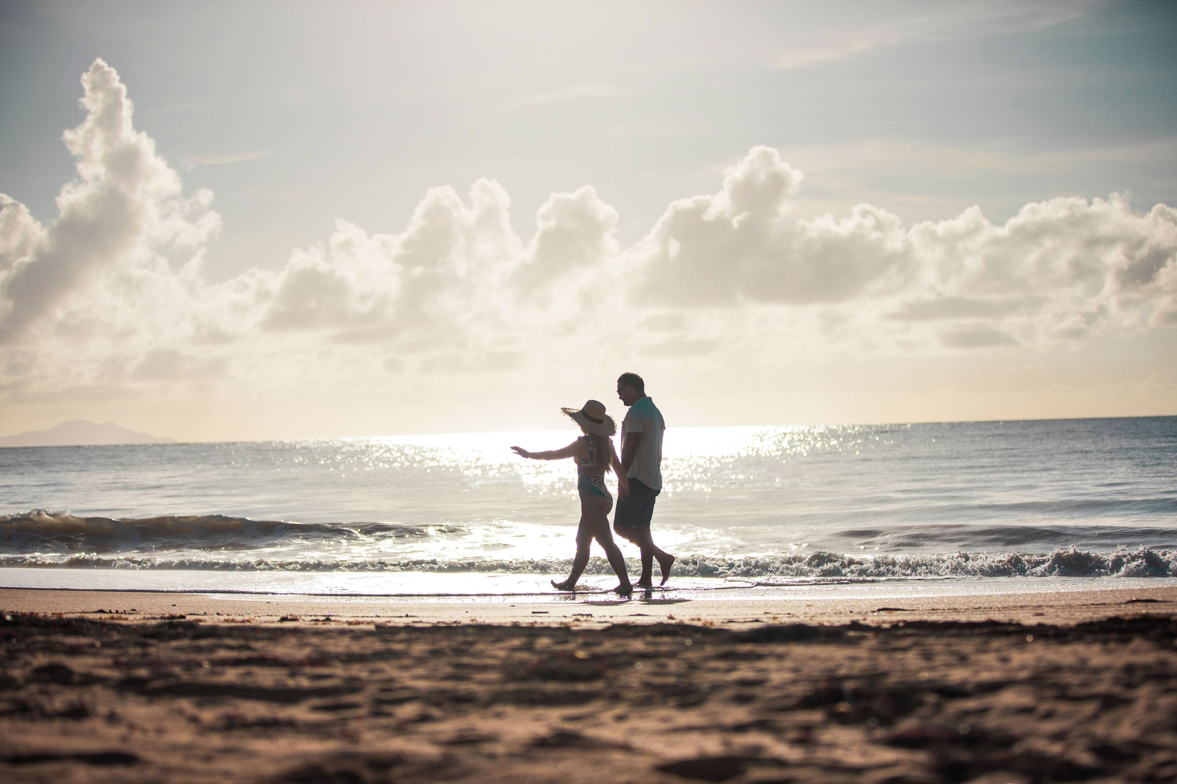 Ein Paar spaziert am Strand, im Hintergrund Meer und ein klarer Himmel.