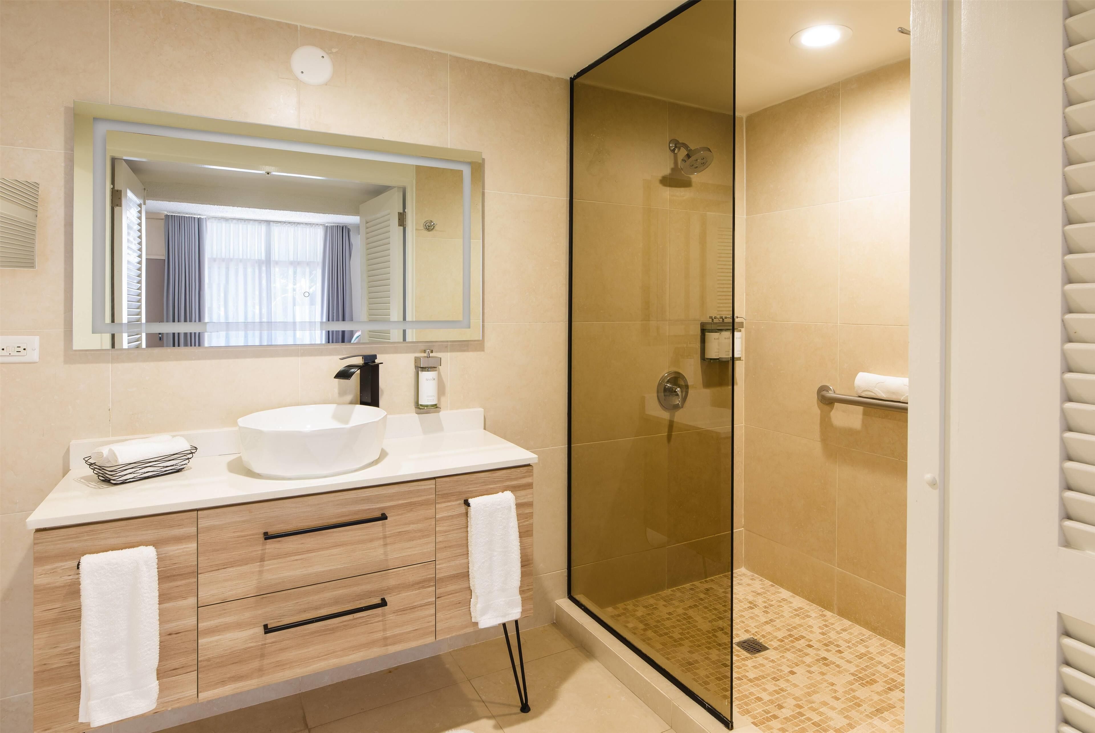 A modern bathroom with a large mirror, a white sink, wooden vanity, and a glass-enclosed shower.