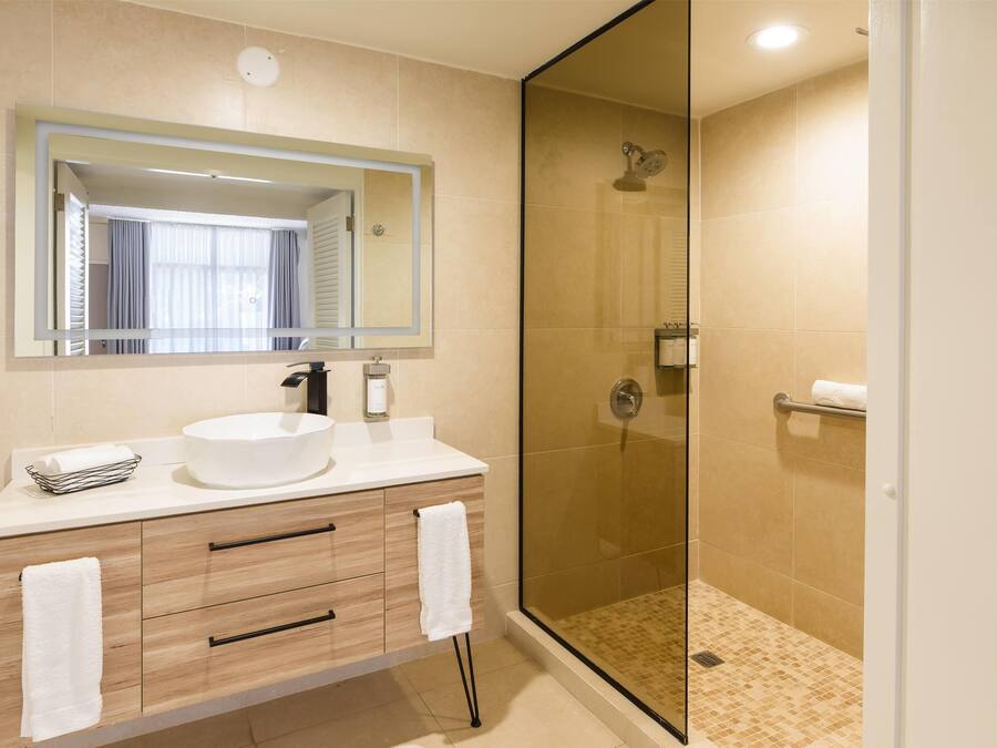 A modern bathroom with a large mirror, a white sink, wooden vanity, and a glass-enclosed shower.