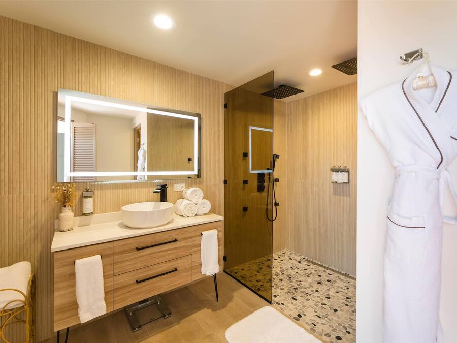 A modern bathroom with a large mirror, wooden vanity, and a walk-in shower.