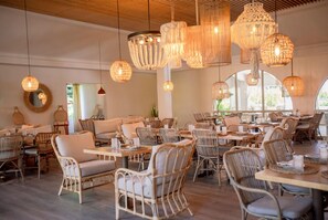 A spacious restaurant with wicker furniture, hanging wicker chandeliers, and large windows. - Wyndham Palmas Beach and Golf Boutique Resort (Humacao)
