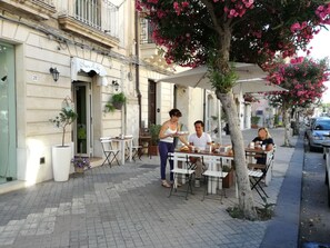 An outdoor cafe with tables and chairs, a waiter serving food, and a building with a cafe named "Cafe Belle." - B&B Luna (Syracuse)
