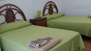 A room with two single beds, each with a green bedspread and a wooden headboard. There is a nightstand with a green lamp and a framed picture on the wall above the beds. - Hostal Las Eras (Cubillos del Sil)