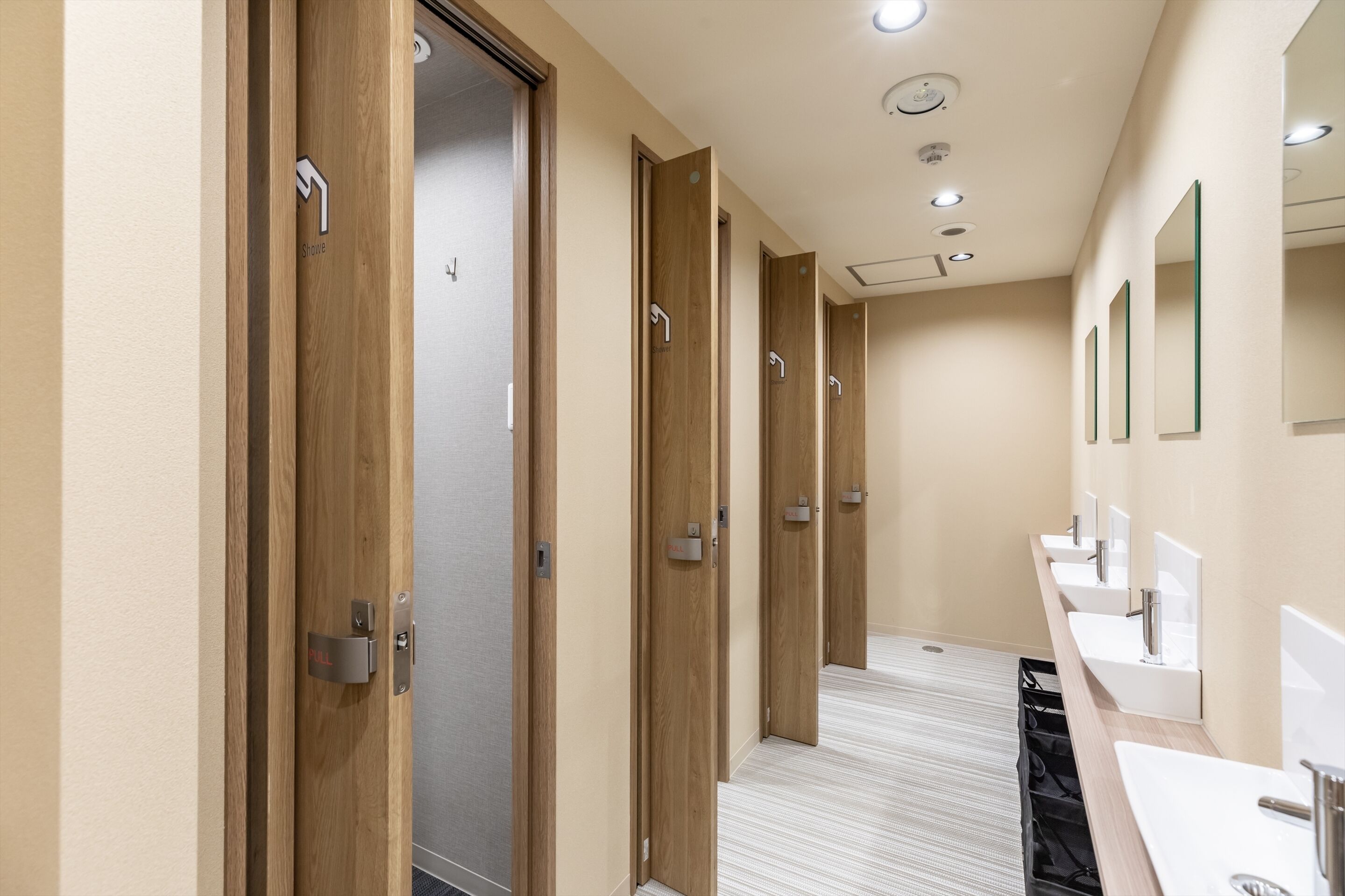 A hotel bathroom with multiple sinks, wooden doors, and a tiled floor.