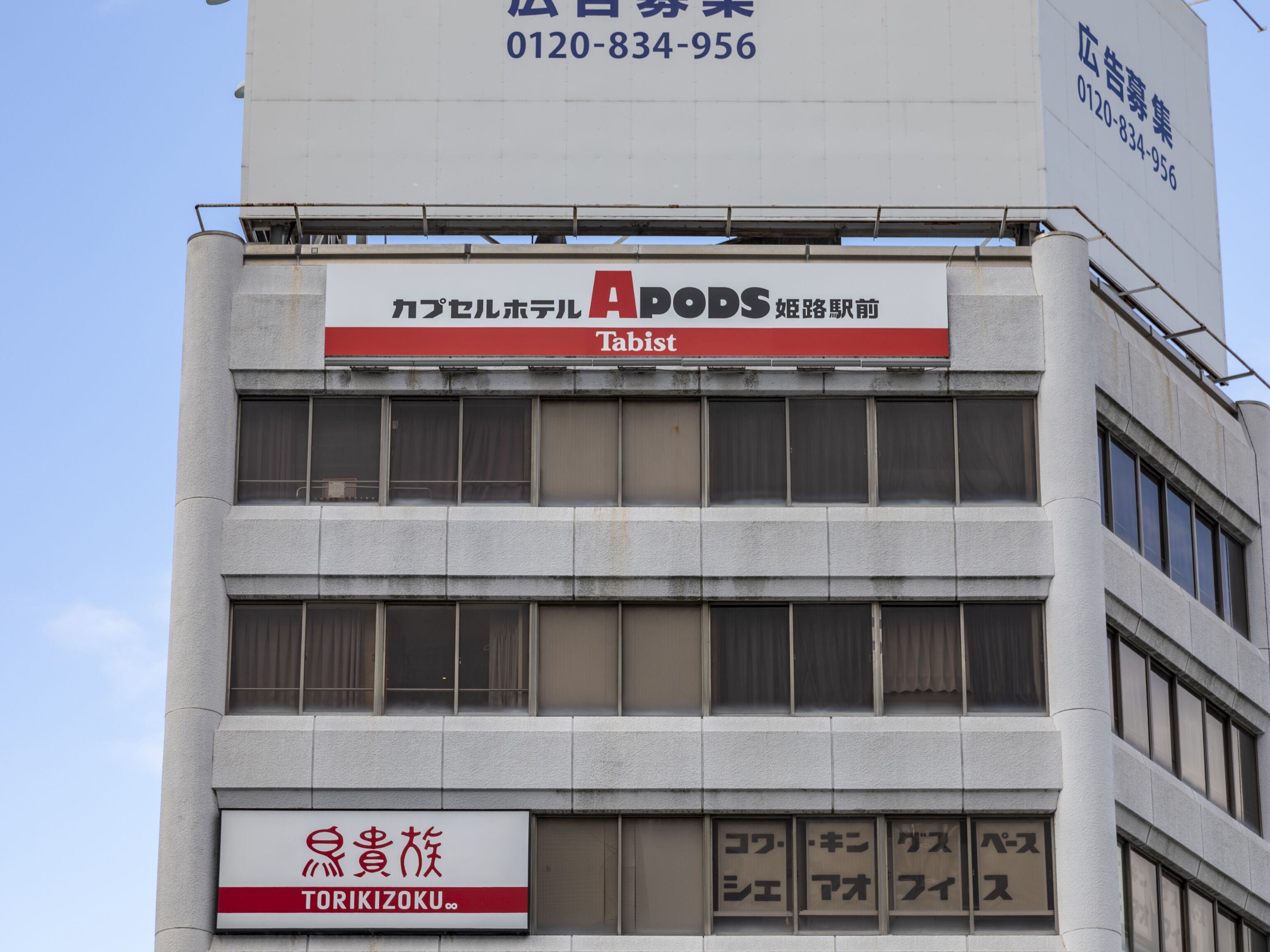 Un edificio con varios letreros, incluyendo uno para 'APODS' y otro para 'TORIKIZOKU'.