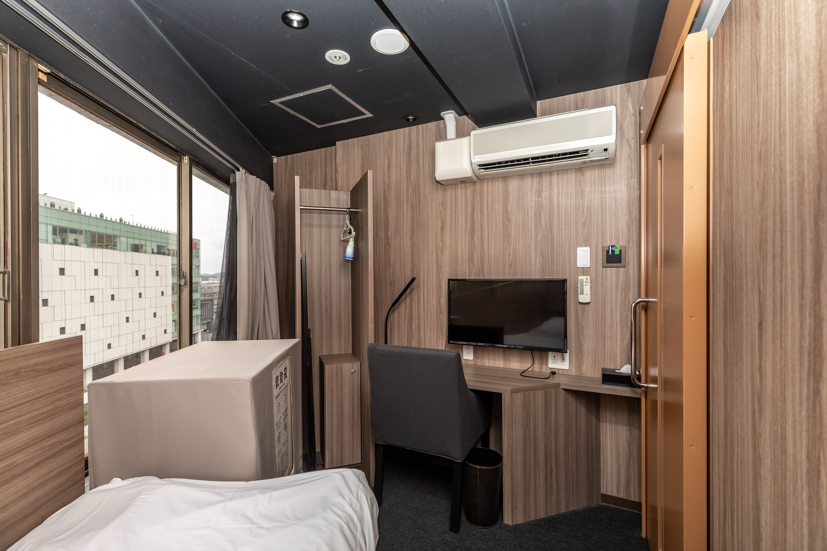 Ein kleines Hotelzimmer mit Bett, Schreibtisch mit Stuhl, Fernseher und Klimaanlage.