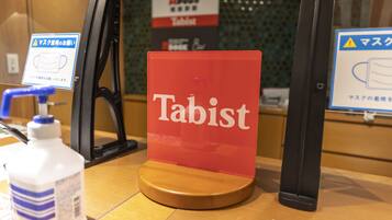 A sign with the word "Tabist" on a wooden table in a room with a green tiled wall.