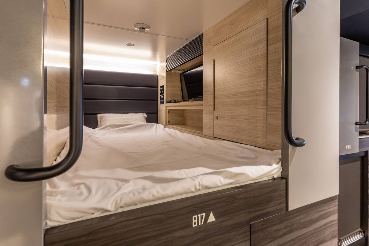 Een compacte, moderne kamer met een bed, ingebouwde opbergruimte en een klein zithoekje.