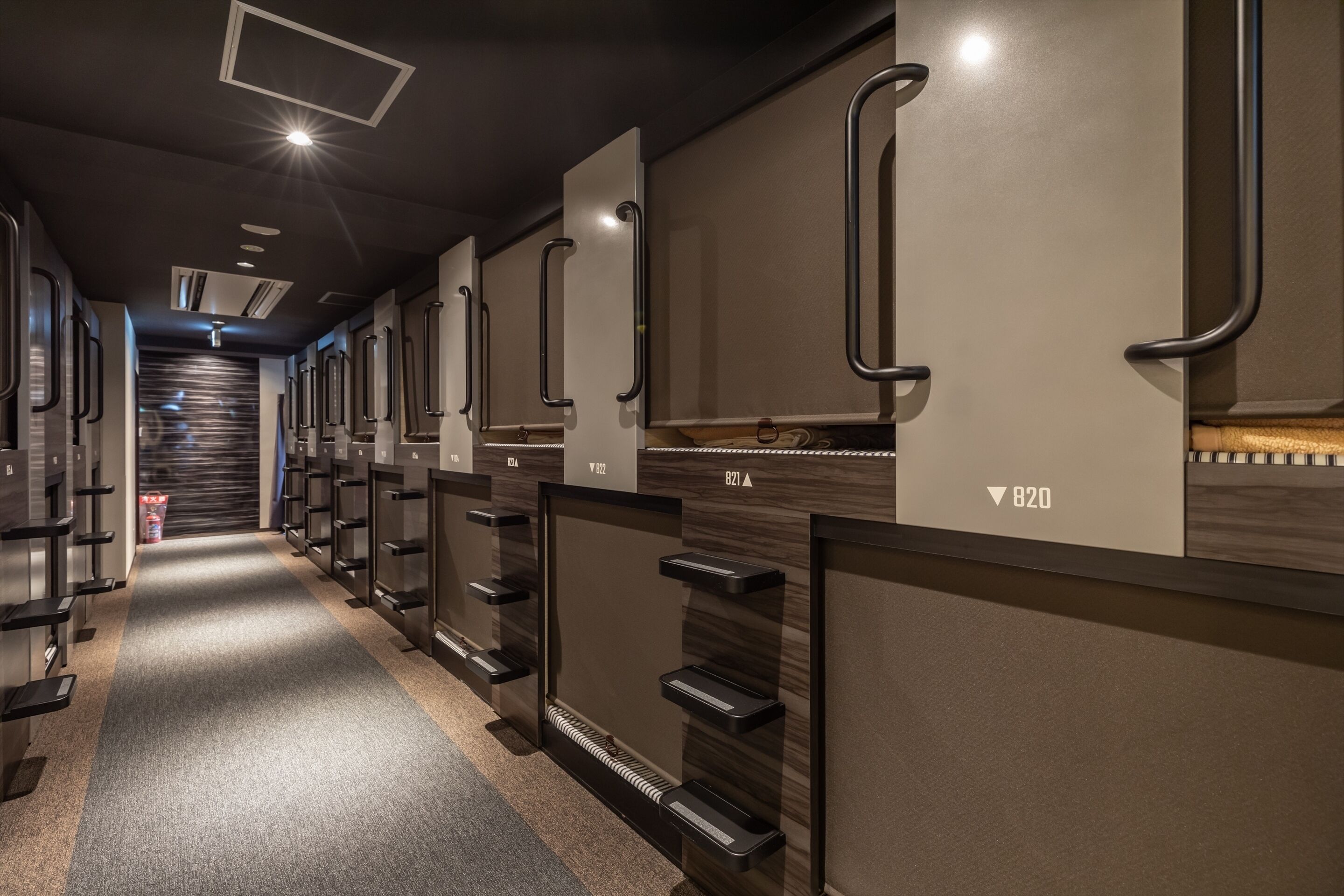 A row of hotel rooms with individual door handles, a carpeted floor, and a staircase in the background.