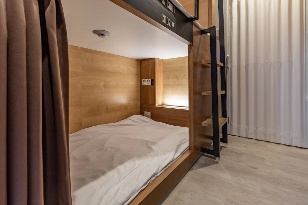 Een stapelbed met een houten hoofdbord en een raam. Daarboven hangt een bordje met het kamernummer.