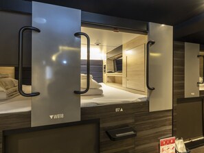 A modern hotel room with a bed, a TV, and a fire extinguisher sign. - Tabist CapsuleHotel APODS Himeji Station (Himeji)