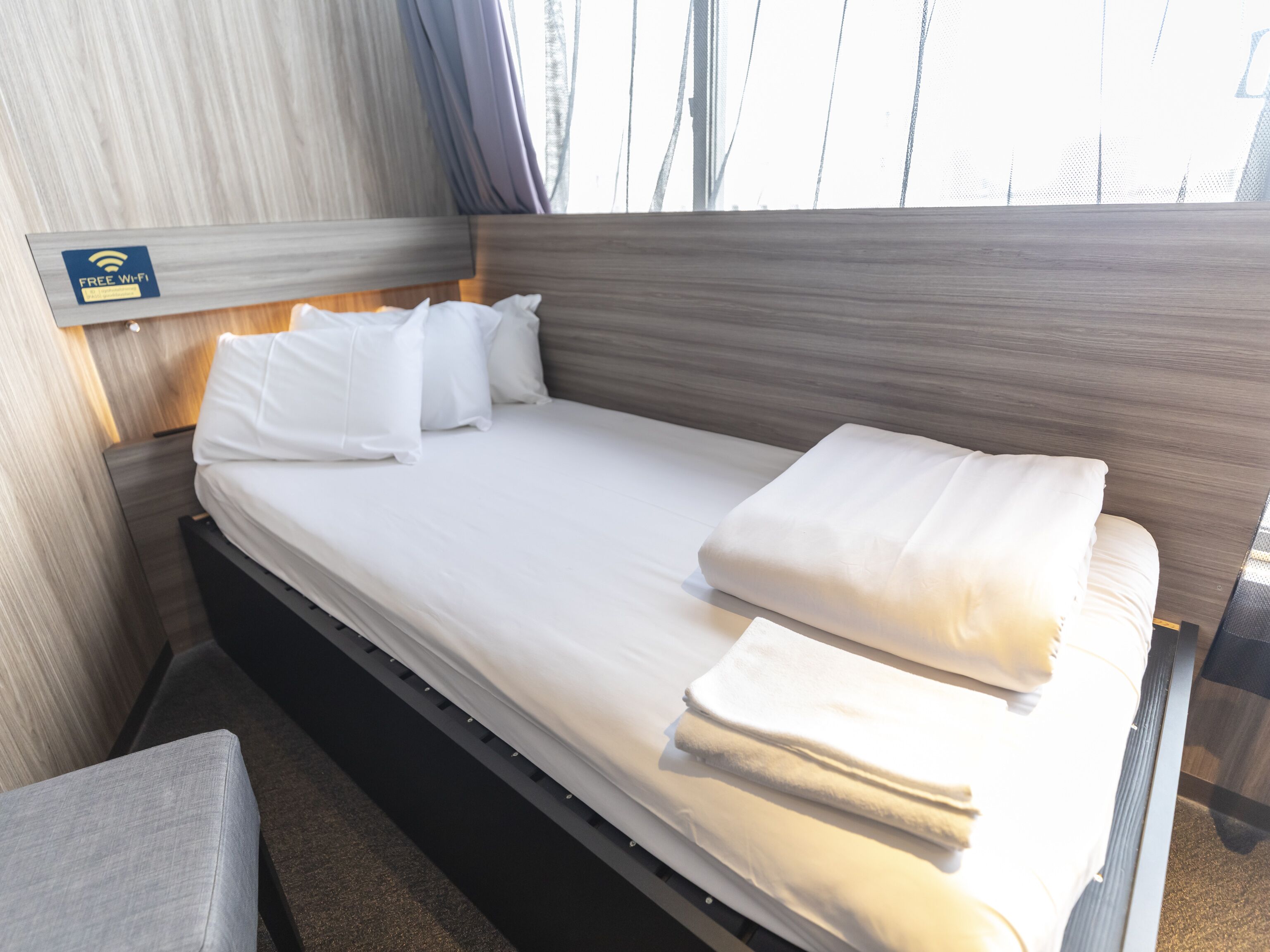 A neatly made bed with white linens and pillows, a wooden headboard, and a sign indicating free Wi-Fi.