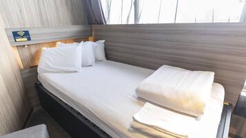 A neatly made bed with white linens and pillows, a wooden headboard, and a sign indicating free Wi-Fi.