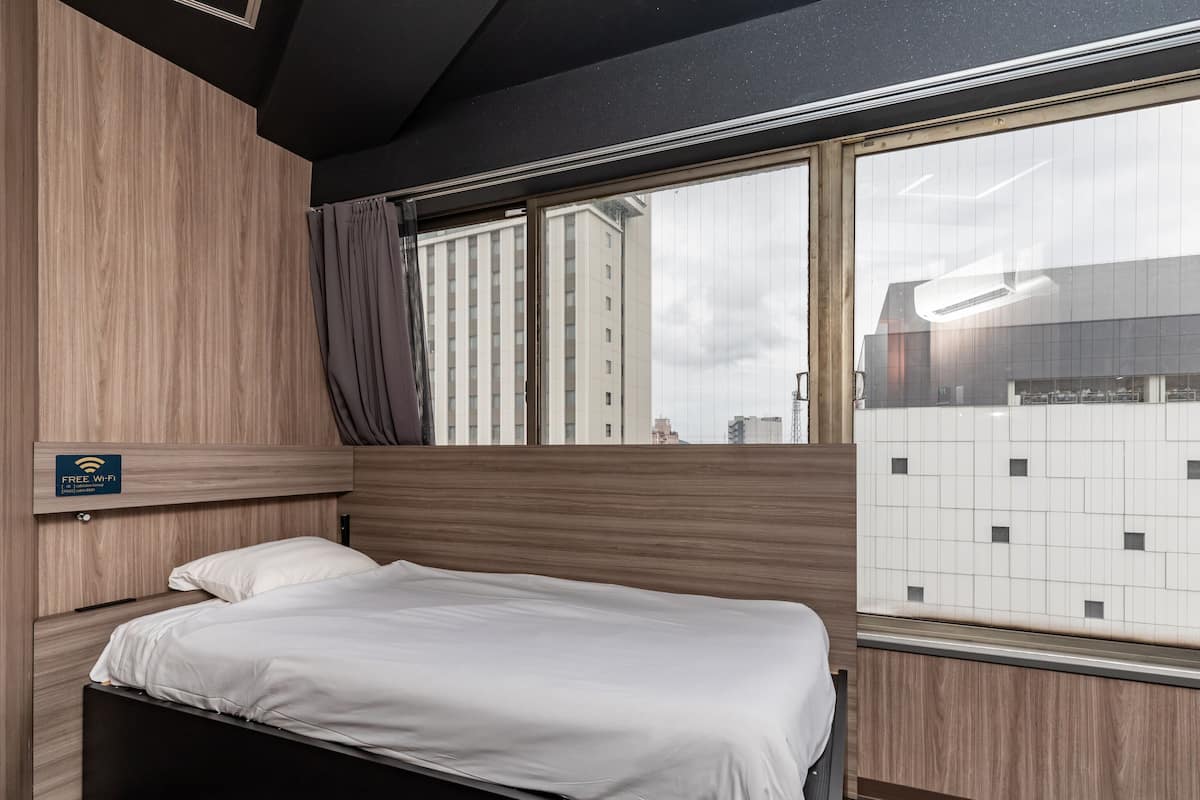 Een hotelkamer met een bed, een raam met uitzicht op gebouwen, en een bordje dat gratis Wi-Fi aangeeft.
