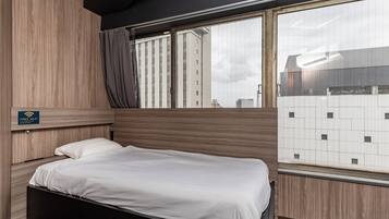 Habitación de hotel con cama, ventana con vista a edificios y un cartel que indica Wi-Fi gratuito.