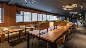 A modern conference room with wooden tables, cushioned seating, and large windows with blinds. - Tabist CapsuleHotel APODS Himeji Station (Himeji)