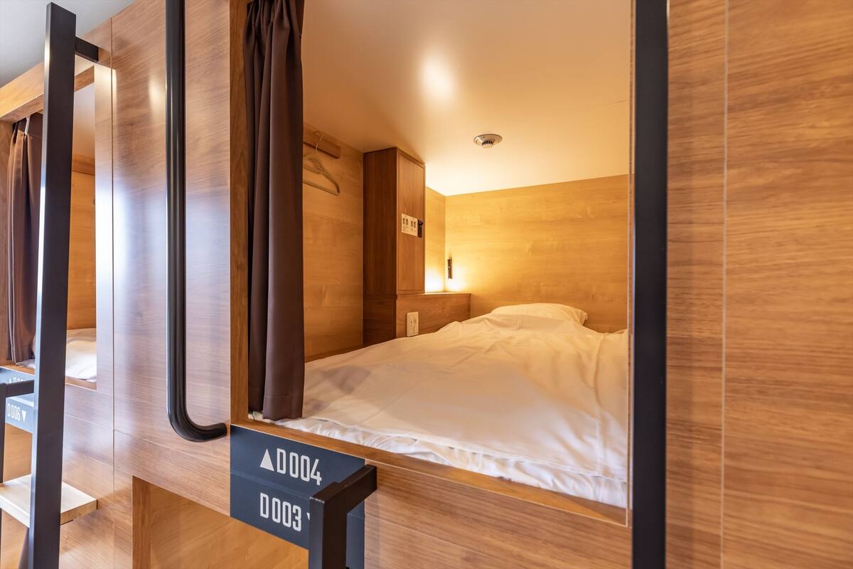 Een moderne hotelkamer met houten details, een bed met witte lakens en een bord met de kamer nummers.