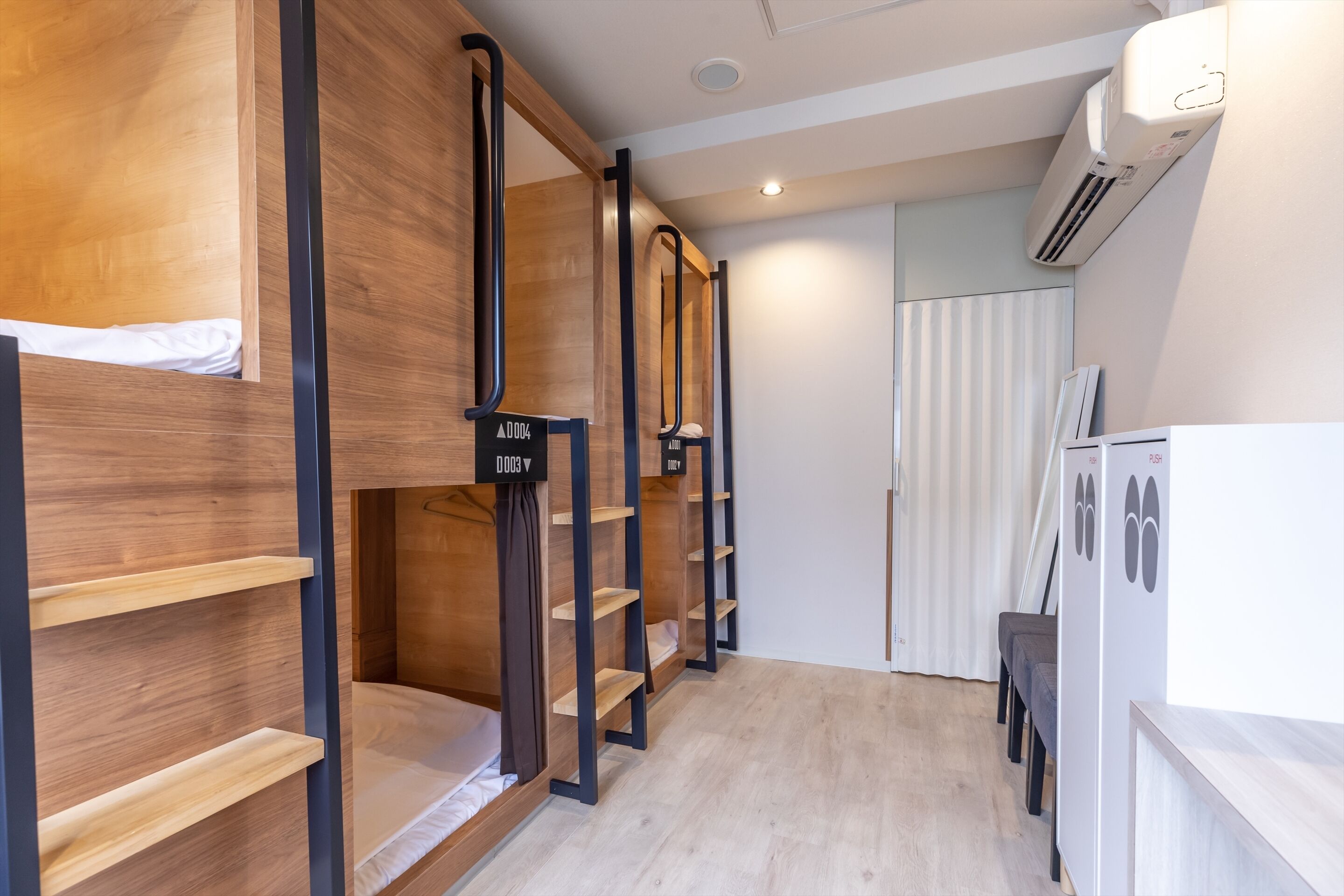 Una habitación de hotel moderna con literas, estantes de madera, un armario blanco y un equipo de aire acondicionado.