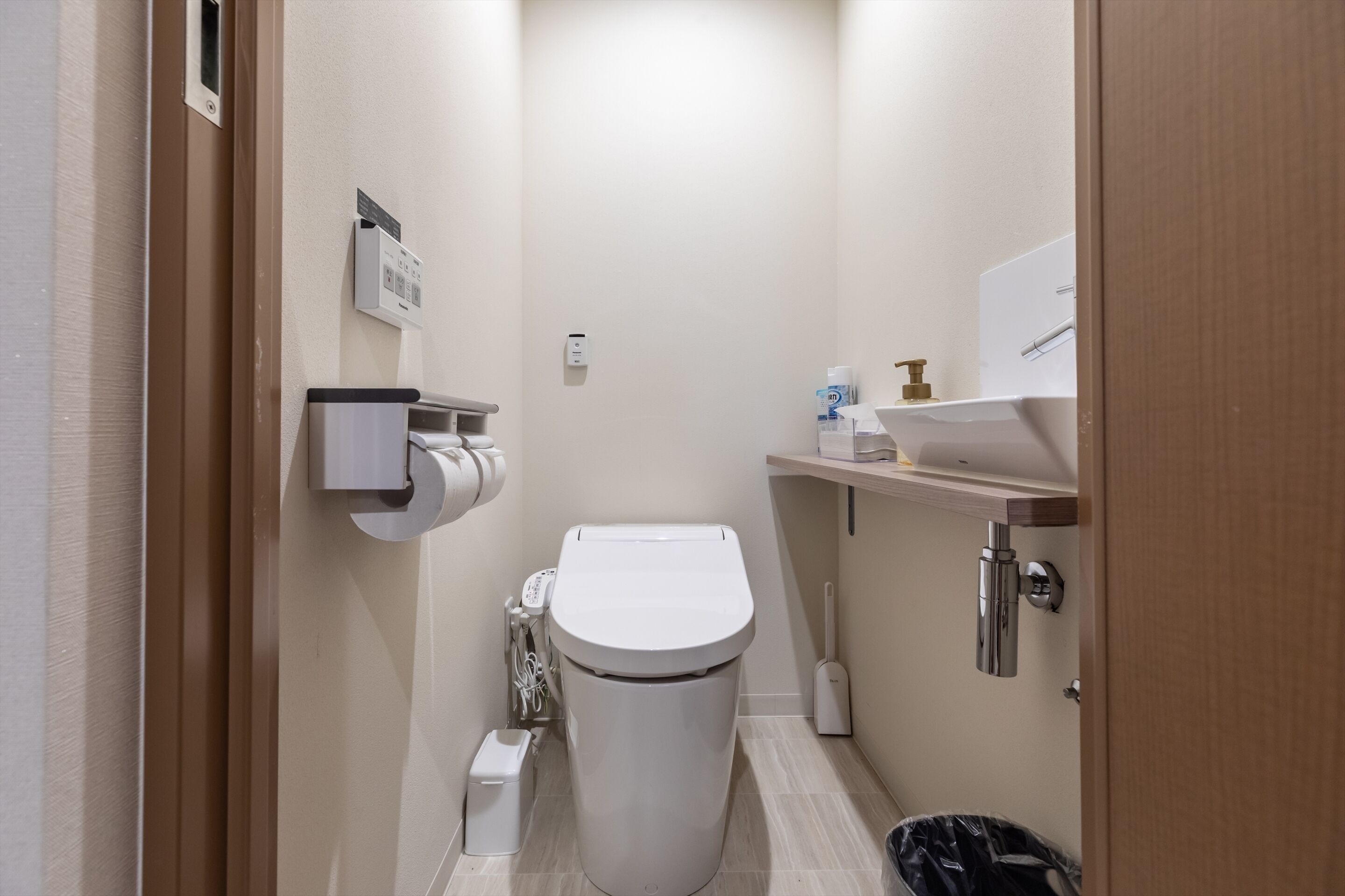 Un baño pequeño y moderno con inodoro, un bote de basura, dispensador de papel higiénico y dispensador de gel antibacterial.