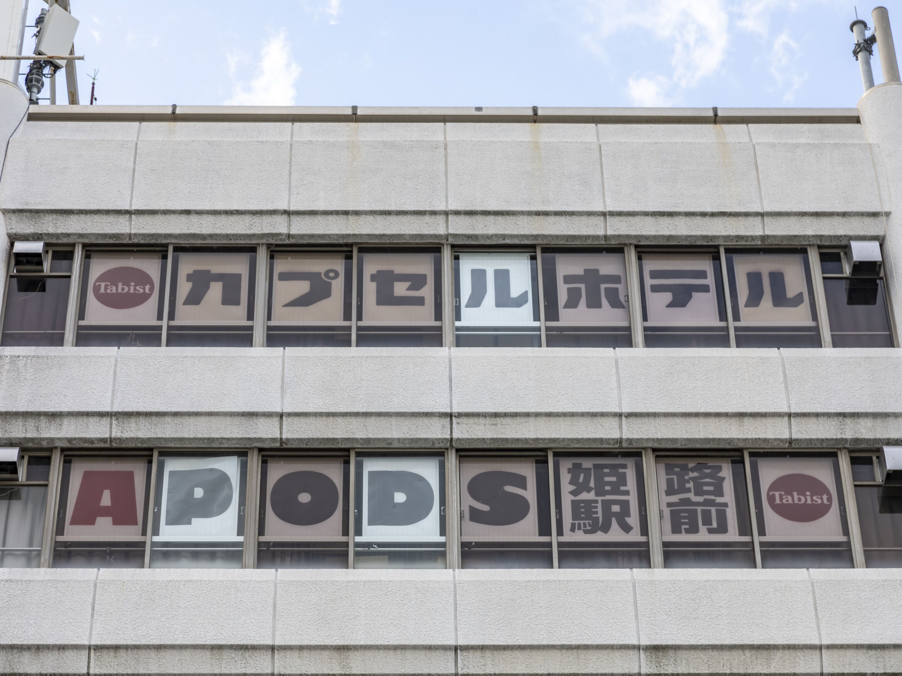 A building facade with large windows displaying various signs, including "Tabist" and "APODS".
