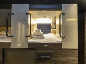 A compact, well-lit room with a bed, a small seating area, and a control panel. - Tabist CapsuleHotel APODS Himeji Station (Himeji)