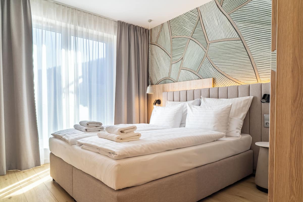 A modern hotel room with a large bed, a wooden headboard, a bedside table, and a wall with a geometric pattern.