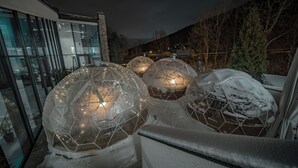 Cupole geodetiche trasparenti illuminate dall'interno, un edificio moderno con ampie finestre e un paesaggio innevato.