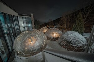 Domes geodésicas transparentes con iluminación interior, un edificio moderno con ventanas amplias y un paisaje nevado.