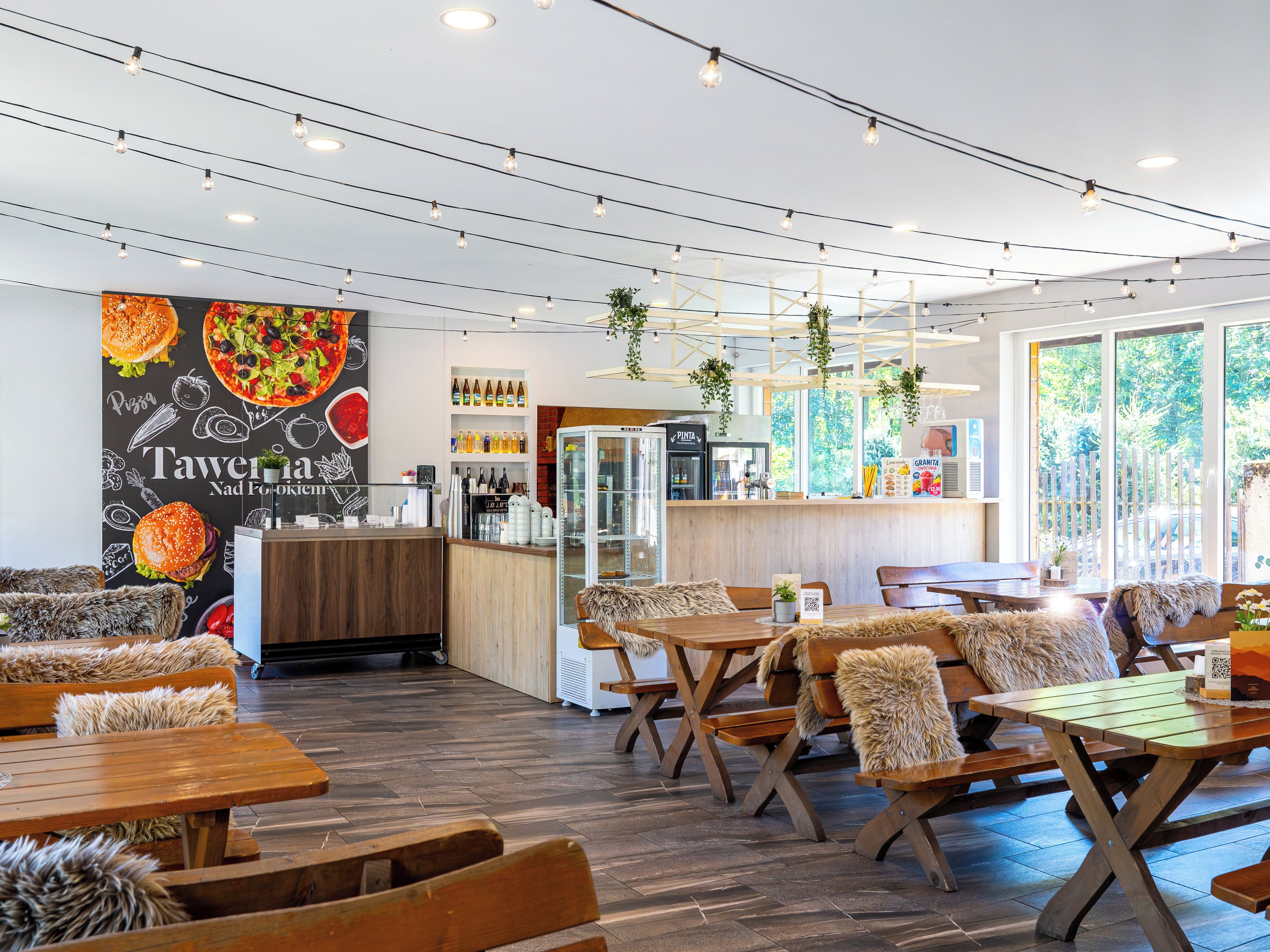 A restaurant interior with wooden tables and benches, a counter with a menu, and a wall with food illustrations.