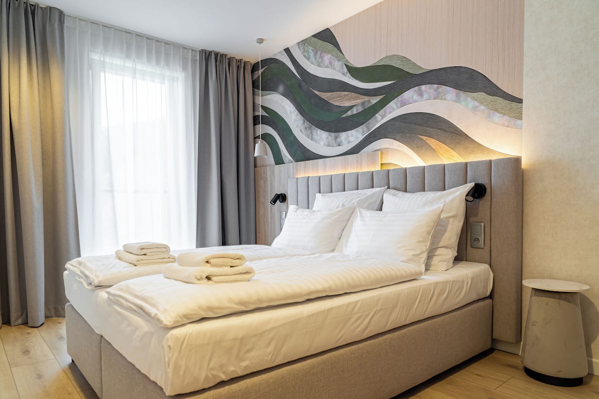 A modern hotel room with a large bed, a headboard with ambient lighting, a bedside table, and a wall-mounted artwork.